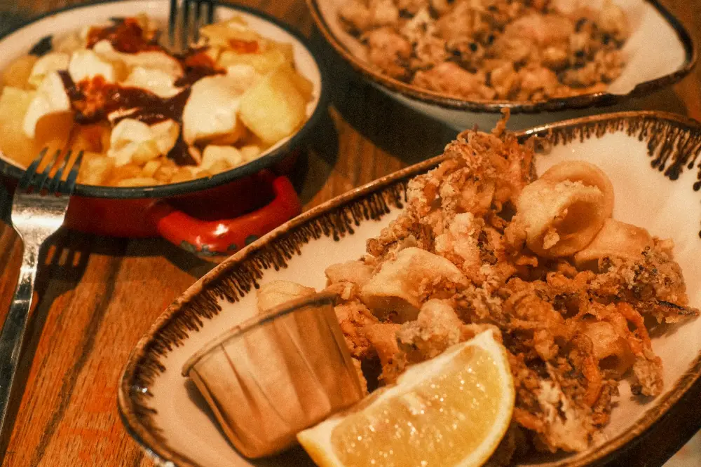 Fuente de calamares con limón y una cazuela de bravas sobre una mesa de barril